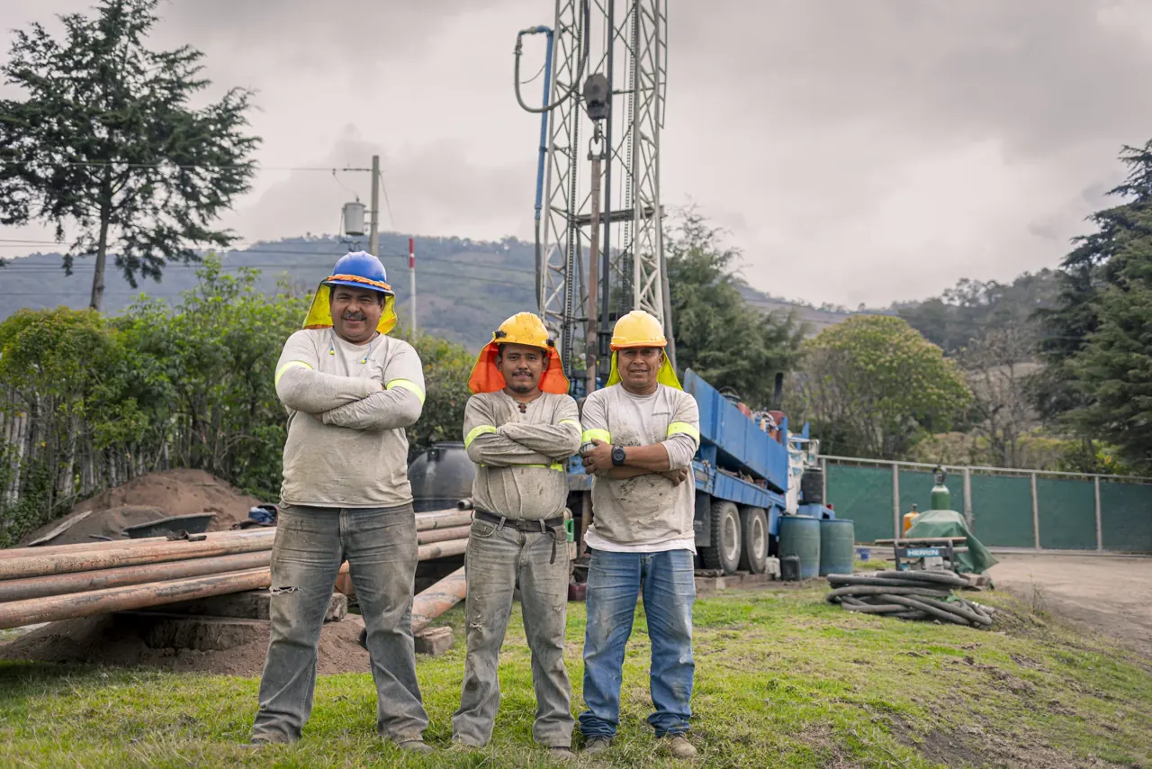 Tres perforistas con cascos junto a la perforadora en el proyecto Pozo Calderas